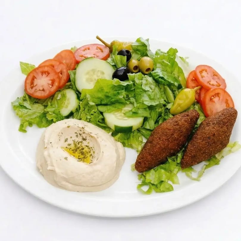 A white plate with a fresh salad, two kibbeh, and a dollop of hummus drizzled with olive oil.